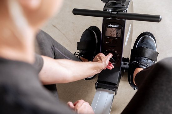 Een vrouw met donkere sportkleding past de weerstand aan op de VirtuFit roeimachine.