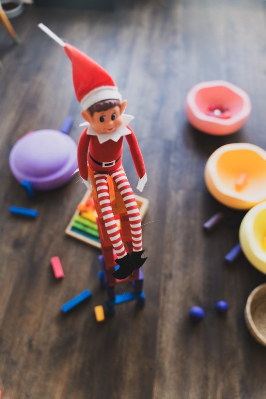 Elf met kerstmuts en gestreepte broek, zittend op een blokkentoren, omringd door speelgoedblokjes.