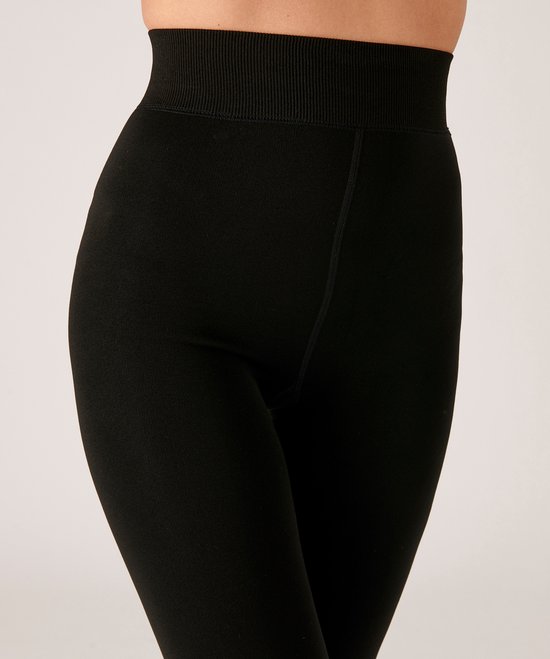 Model in zwarte legging met opgeruwde tailleband, zittend.