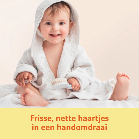 Lachende baby in een witte badjas met capuchon, vasthoudend een haarborsteltje.