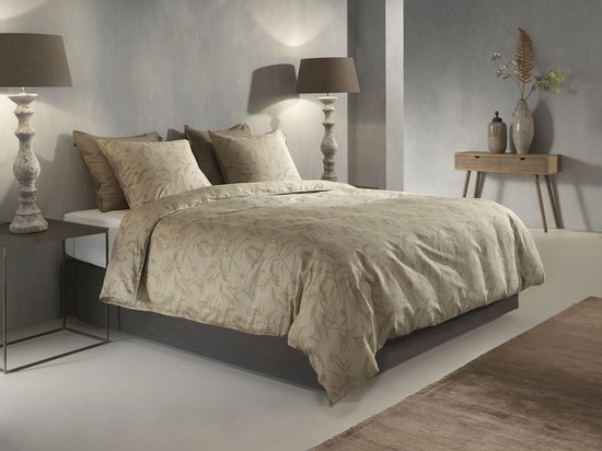Slaapkamer met een opgemaakt beige dekbedovertrek met bladermotief, lampen en bijzettafels.