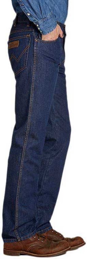 Zijaanzicht van een donkerblauwe Wrangler-spijkerbroek met contrasterende stiksels en bruine schoenen.