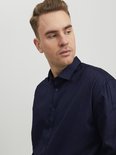 Man draagt een donkerblauw overhemd met lange mouwen en kijkt weg van de camera.