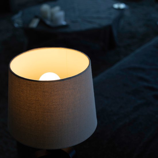 Een aanstaande lamp met een beige kap verlicht een ruimte in de avond.