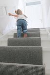 Klein meisje met blonde staartjes en gestreepte broek loopt trap op.