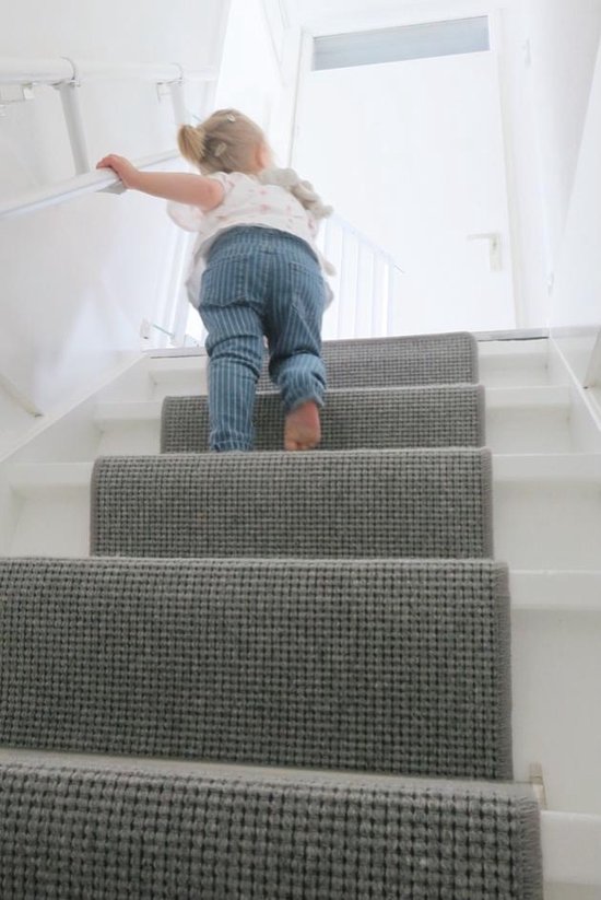 Klein meisje met blonde staartjes en gestreepte broek loopt trap op.