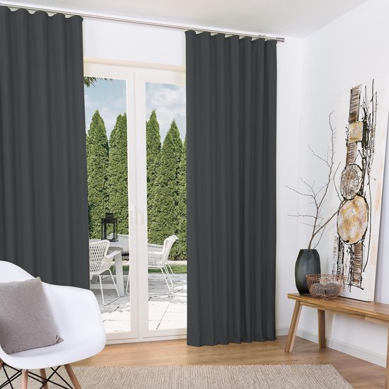 Antracietgrijze gordijnen hangen voor een glazen schuifdeur naar een tuin, in een woonkamer.