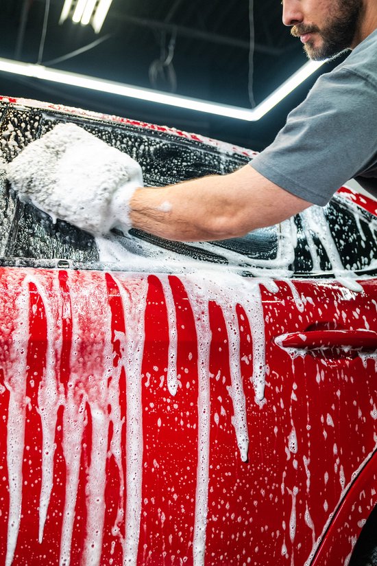 Man wast rode auto met schuimende shampoo en spons. Close-up op portier en raam.