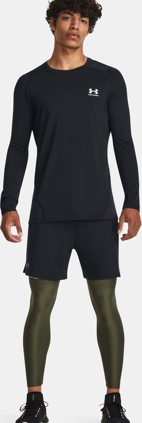 Model draagt een zwarte Under Armour shirt met lange mouwen, zwarte short en olijfgroene sportlegging.