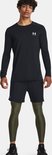 Model draagt een zwarte Under Armour shirt met lange mouwen, zwarte short en olijfgroene sportlegging.