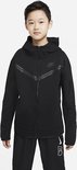 Jongen met een zwart Nike Tech Fleece vest met capuchon, de Nike logo is zichtbaar.