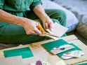 Oranje Fiskars schaar knipt in bruine enveloppen, met groene en bruine papieren op tafel.