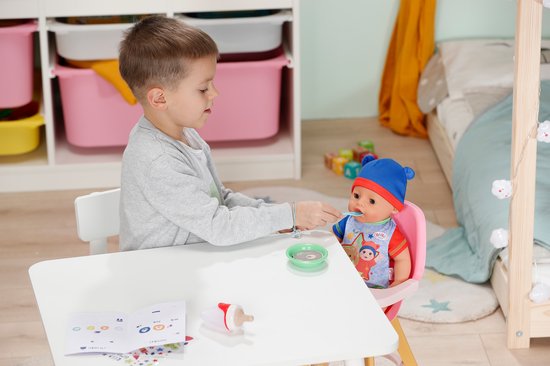 Jongen voert BABY born Jonas pop, die in een roze stoel zit, met een lepel uit een schaaltje.
