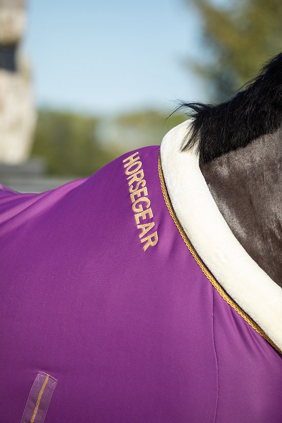 Close-up van paarse zweetdeken met gouden bies en Horsegear logo op de nek.