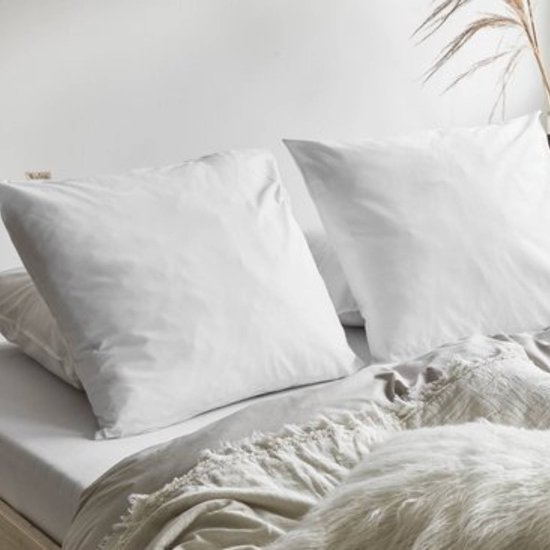 Twee witte kussenslopen op een bed, met een plaid en sierkussen.