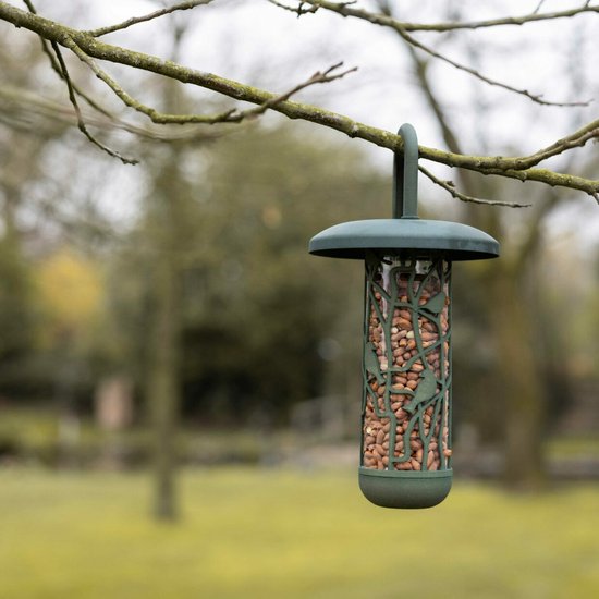 Donkergroene notensilo met een open, takachtig ontwerp met gestileerde vogels, gevuld met pinda's en hangend aan een boomtak.