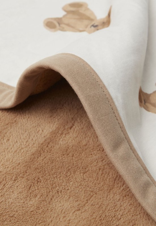 Détail du bord retourné d'une couverture pour bébé, montrant une couche de coton blanche à imprimé ours en peluche et une doublure en polaire marron.