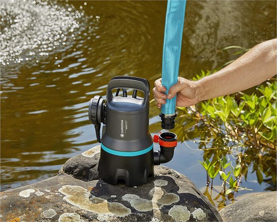 Zwarte en turquoise dompelpomp met handvat, aangesloten op een blauwe slang, op een steen aan het water.