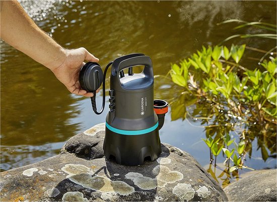 Hand plaatst Gardena vuilwaterpomp op een rots bij het water.