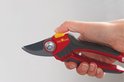 Hand met snoeischaar: rood-grijze soft-inleg handgrepen, gele ontgrendelknop, metalen snijblad.