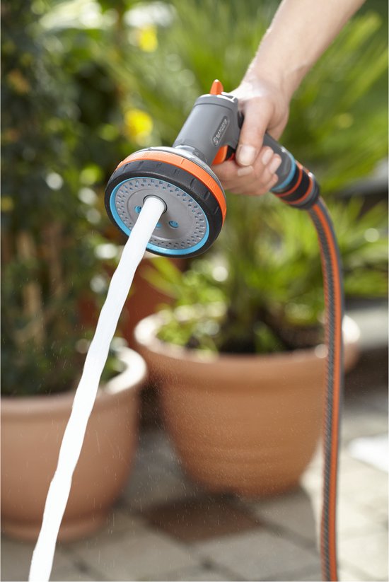 Een hand houdt een grijze Gardena sproeikop vast, met een krachtige waterstraal gericht naar beneden.