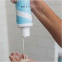 Een hand pakt een fles met de tekst 'BOUCLÈME' terwijl er product uitloopt in een andere hand.