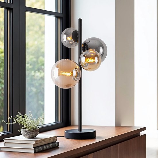 Lampe de table noire avec quatre sphères en verre (deux ambre, deux fumé) sur un pied élancé, placée sur un buffet en bois.