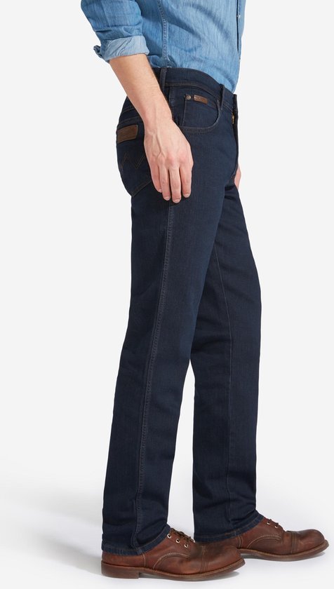 Zijaanzicht van een donkerblauwe Wrangler jeans met regular fit, gedragen met bruine schoenen.