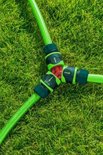 Groene tuinslangkoppelingen met groen en donkergroen Y-verdeelstuk op gras.