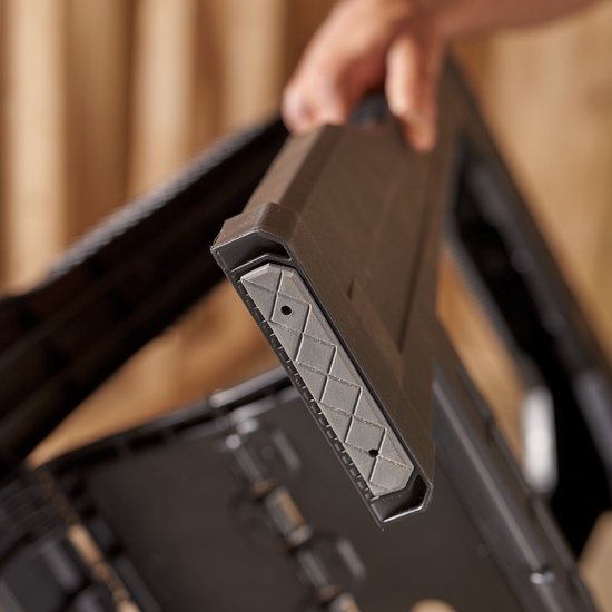 Hand toont rubberen antislip detail van een zwarte Stanley zaagbok.