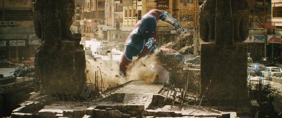Noah Centineo als Atom Smasher, in een rood en blauw pak, die door puin breekt in een stad.
