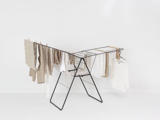 Een zwart Brabantia HangOn droogrek met beige en witte kleding, waaronder handdoeken en shirts, hangend aan wasknijpers en een kledinghanger.