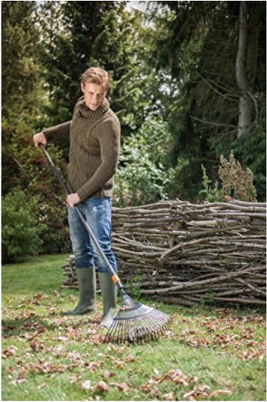 Man met een groen kabeltrui en blauwe jeans hark met een Fiskars bladhark.