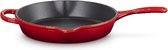 Een rode gietijzeren diepe koekenpan van Le Creuset, schuin van achteren gezien. De pan heeft een zwarte binnenkant en een lange steel.