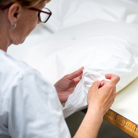 Een vrouw met bril en witte jas bekijkt de textuur van een wit dekbed.