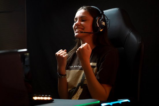 Vrolijke jonge vrouw met een JBL Quantum headset, juichend tijdens het gamen.