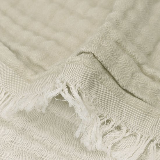 Detail van een groene mousseline deken met rafels en textuur.