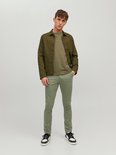 Model staand, draagt een olijfgroene chino broek met groen jack en t-shirt.