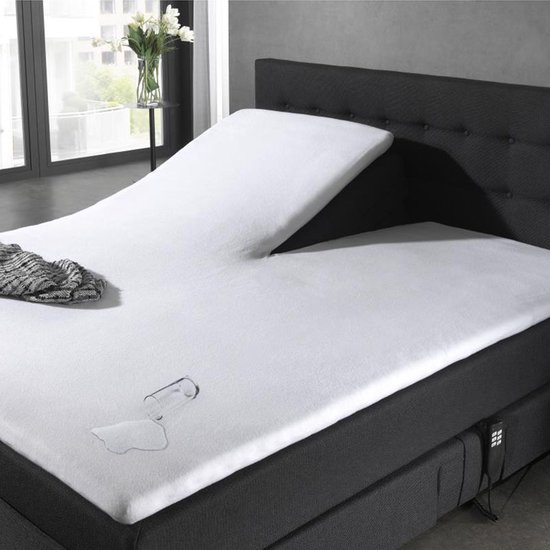 Wit waterdicht molton splittopper hoeslaken op een verstelbaar donkergrijs bed met een omgevallen glas en plasje water.