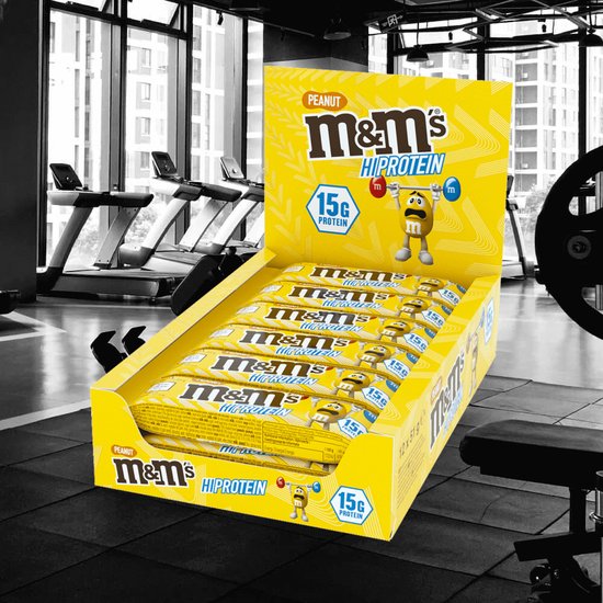 Displaydoos met M&M's Hi Protein Peanut repen in een fitnessruimte.