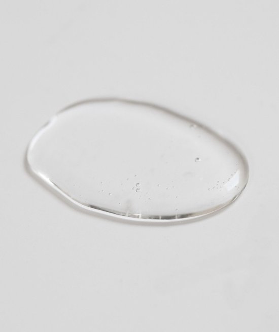 Een doorzichtige, ronde druppel product met kleine luchtbelletjes op een lichte ondergrond.