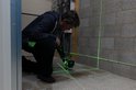 Man met ProXtar kruislijnlaser op een statief, projecteert groene laserlijnen op een betonnen muur en vloer.