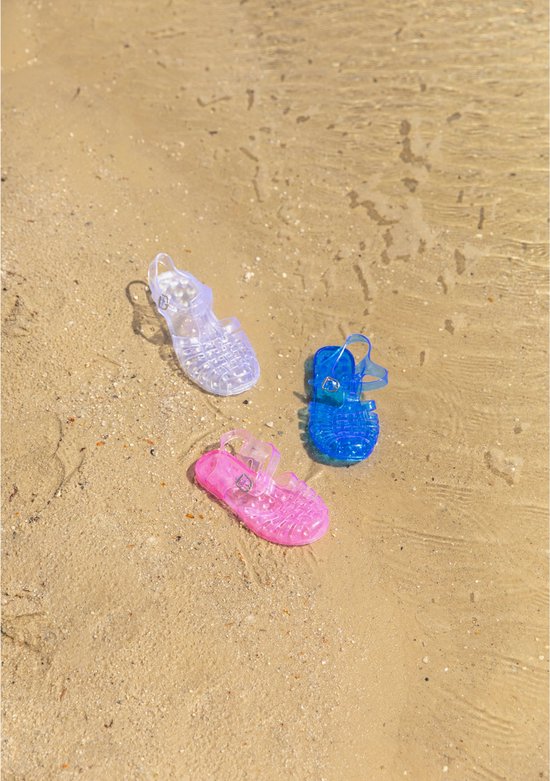Drie transparante waterschoenen in blauw, roze en paars op zanderig strand.