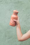 Kind houdt roestbruine drinkfles met stippen en kattengezicht vast.