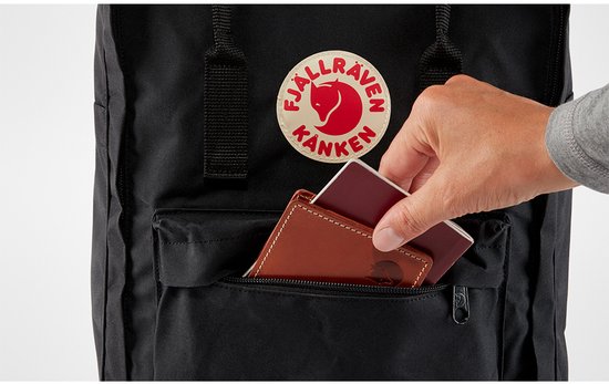 Hand plaatst portemonnee en paspoort in het voorvak van een zwarte Kånken.