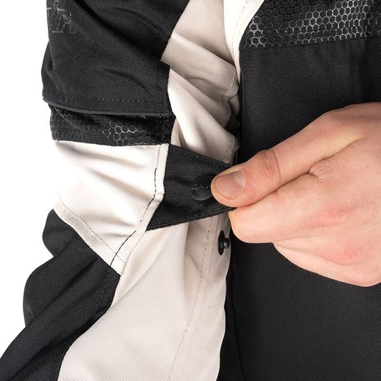 Hand sluit een drukknoop op de zwarte jas met beige mouwen en delen.