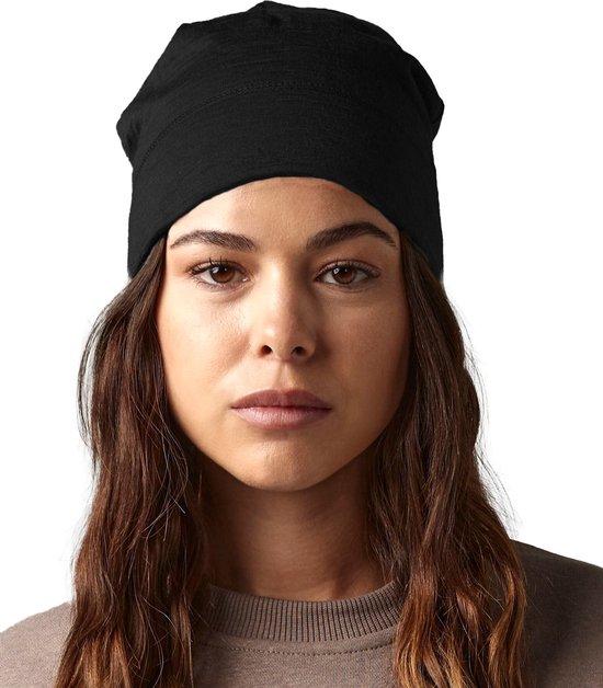 Een vrouw met bruin haar draagt een zwarte beanie van merino wol.