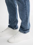 Close-up van de broekspijpen van een man in een lichtblauwe jeans en witte sneakers.
