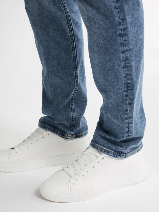 Close-up van de broekspijpen van een man in een lichtblauwe jeans en witte sneakers.