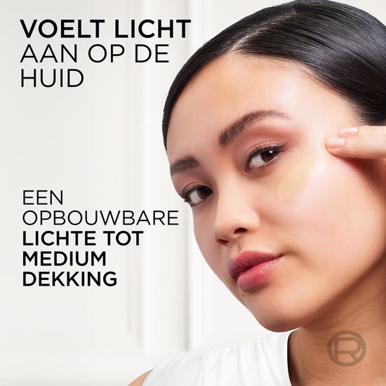 Een vrouw met donker haar brengt foundation aan op haar wang.